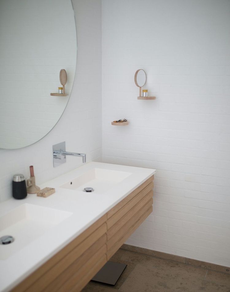 Bathroom with a large round mirror, white sink, and wooden cabinet. Small shelf with a mirror and items on the wall.