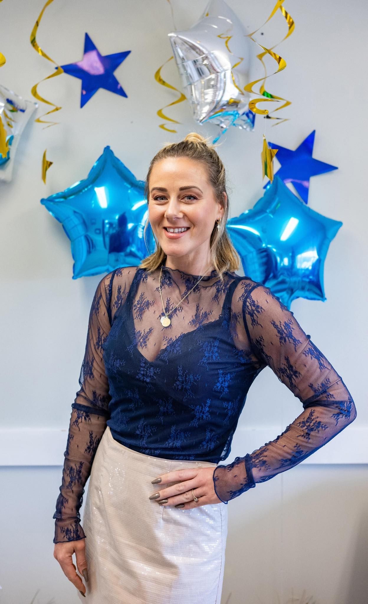 A woman is standing in front of a wall with blue balloons and stars.