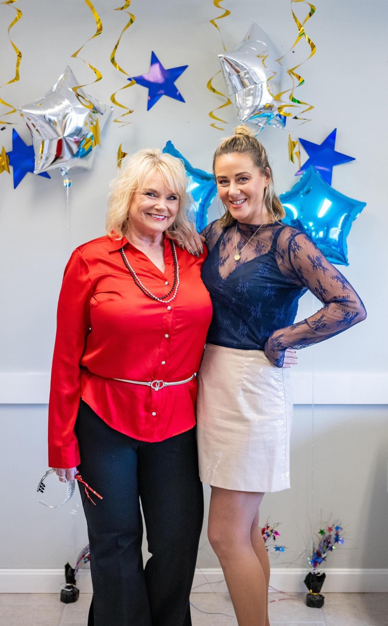Two women are posing for a picture in front of balloons.