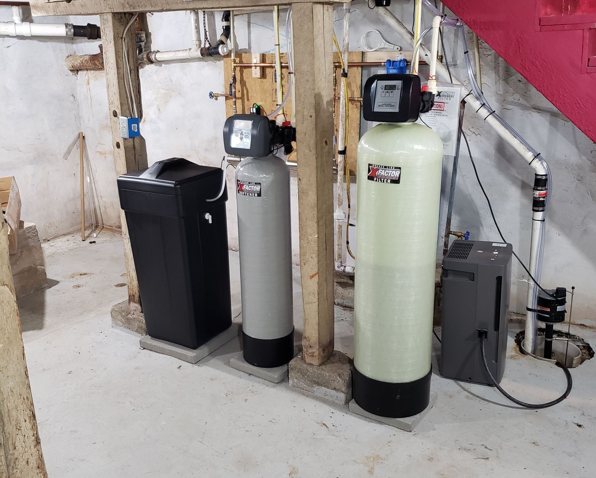 Three water filters are sitting in a basement next to a staircase.
