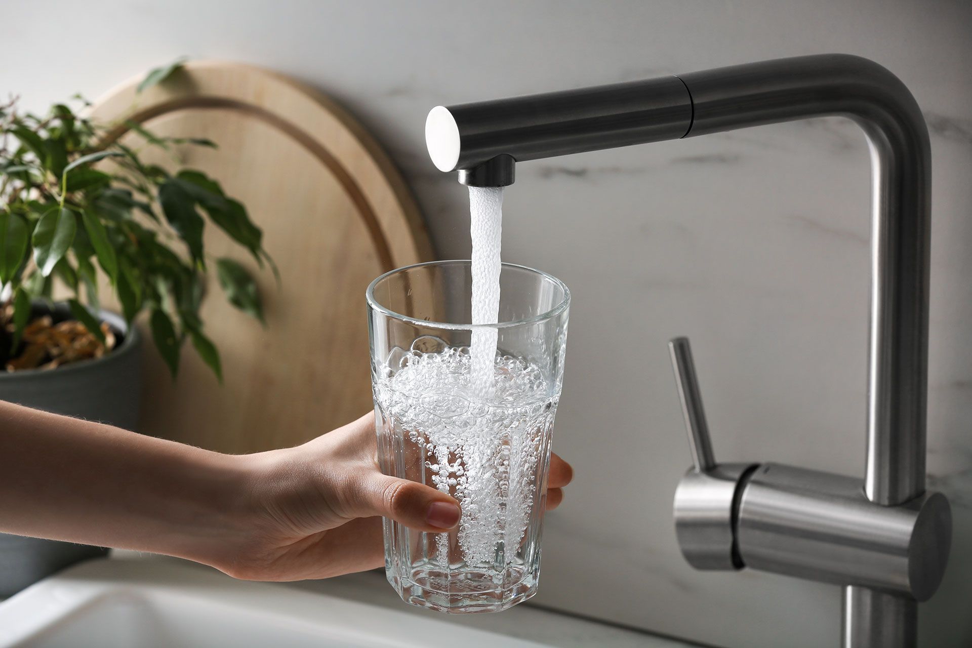 A person is pouring water into a glass from a faucet.