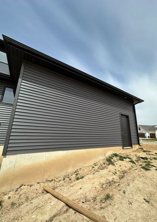 A house with a black siding is sitting on top of a dirt hill.