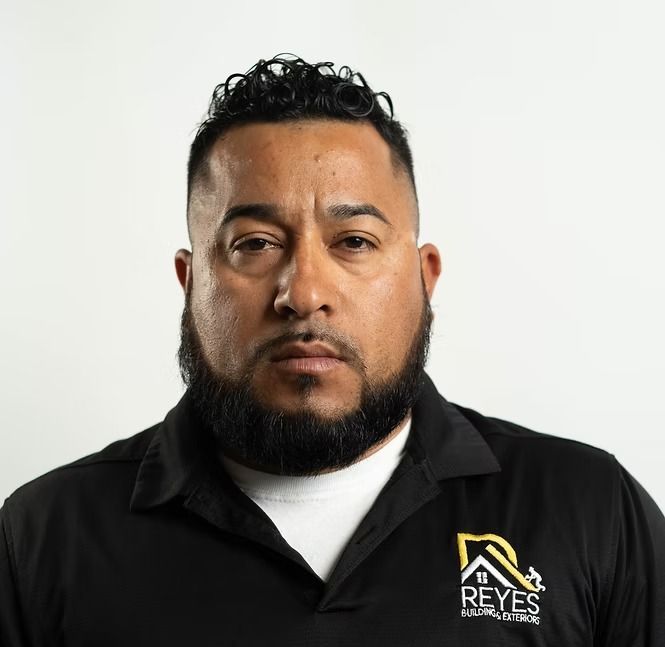 A man with a beard is wearing a black shirt that says reyes on it.