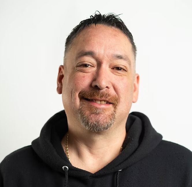 A man with a beard is wearing a black hoodie and smiling.