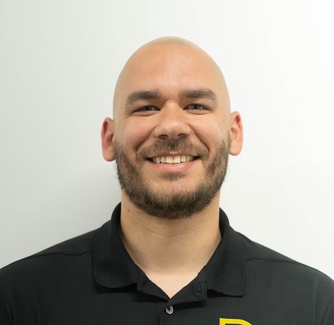A bald man with a beard is wearing a black shirt and smiling.