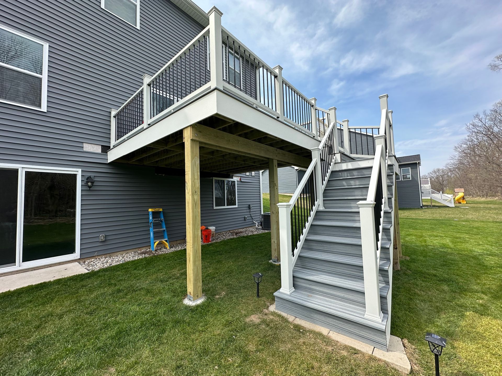 A large deck with stairs leading up to it is in the backyard of a house.