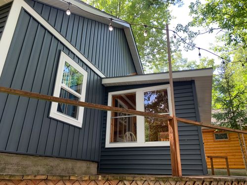 A small house with a blue siding and white trim is surrounded by trees.