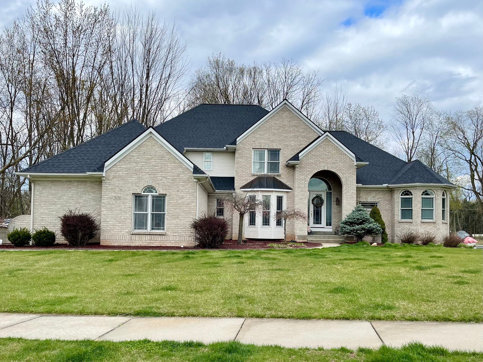 A large brick house with a black roof is sitting on top of a lush green lawn.