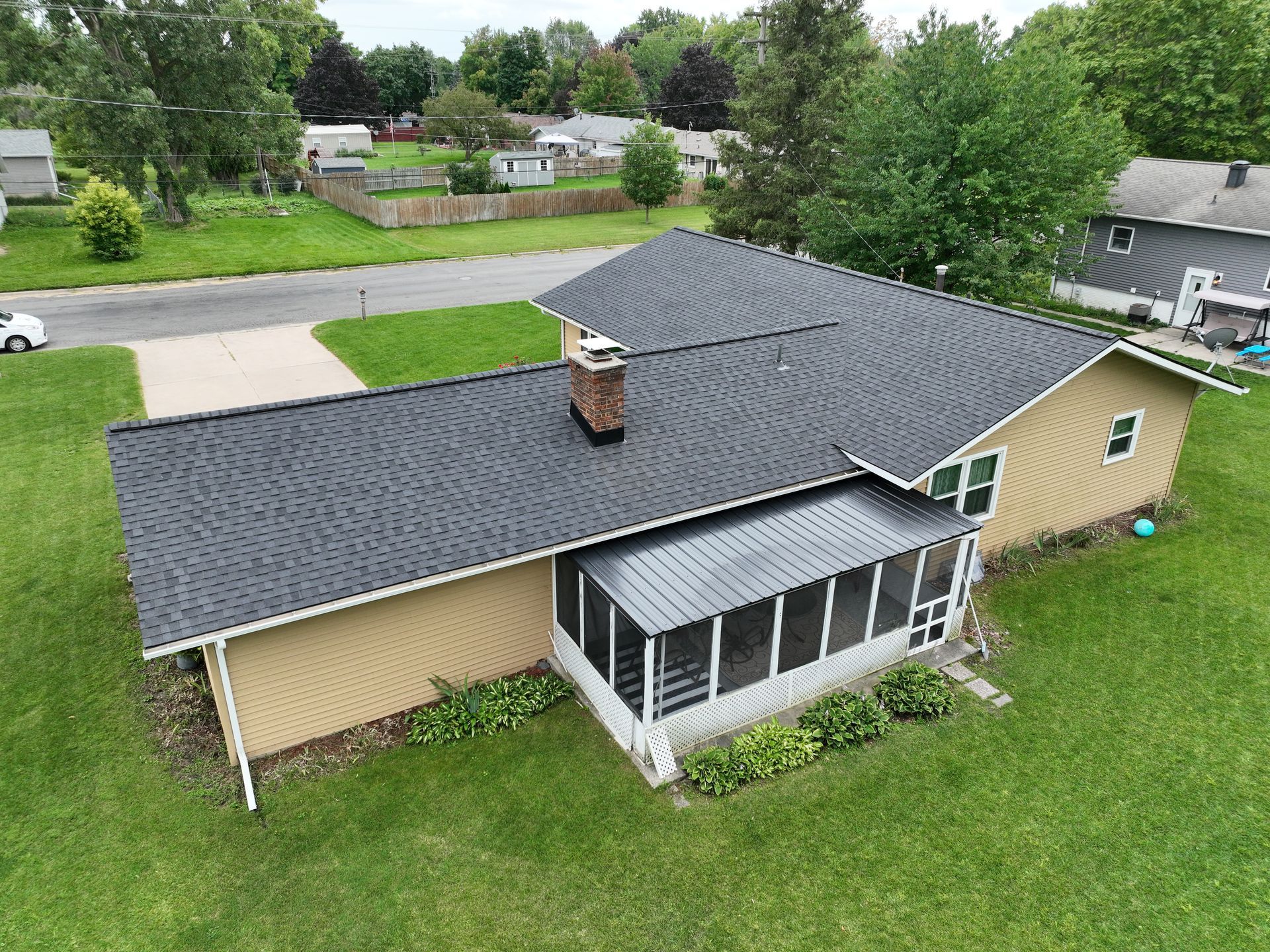 An aerial view of a house with a screened in porch and a black roof.