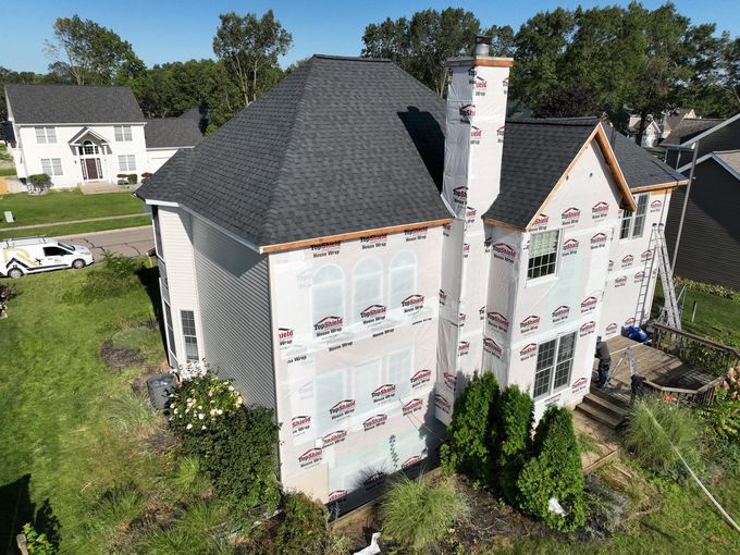 A house being renovated, with a new roof and wrapped in protective material. A chimney and ladder are visible.