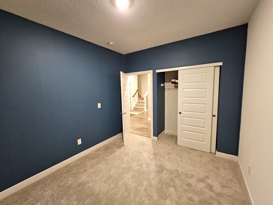 An empty bedroom with blue walls and a closet.