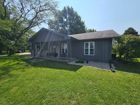 A gray house with a porch and a lot of grass in front of it.