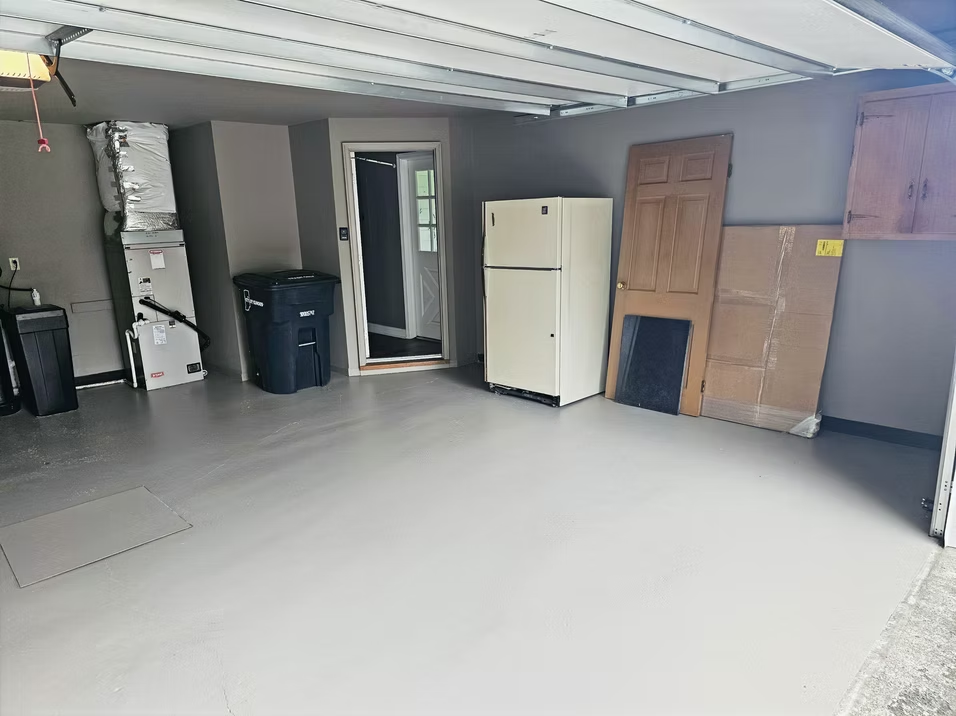 A garage with a refrigerator and a trash can in it.