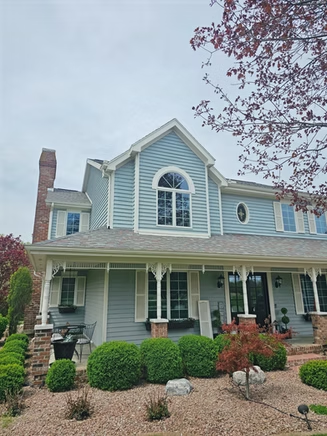 A large blue house with a large porch and a brick chimney.