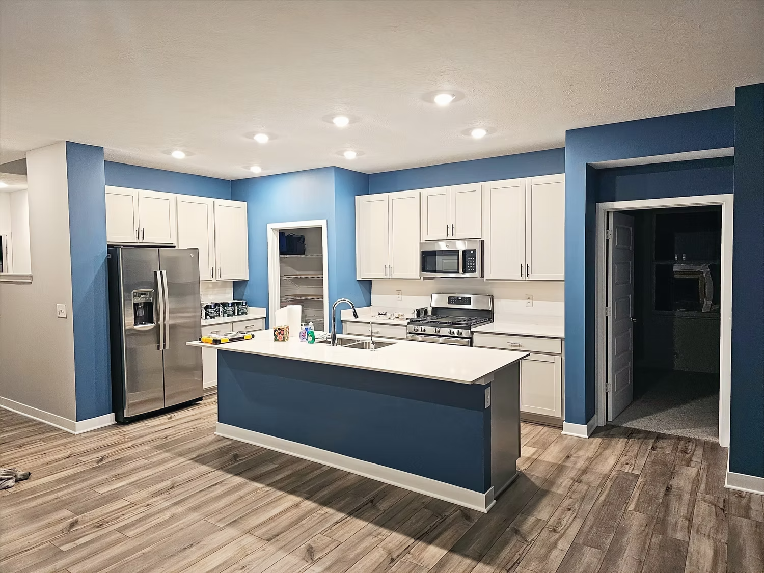 A kitchen with blue walls , white cabinets , stainless steel appliances and a large island.