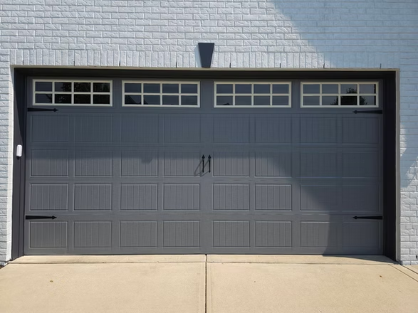 A gray garage door is sitting in front of a white brick building.