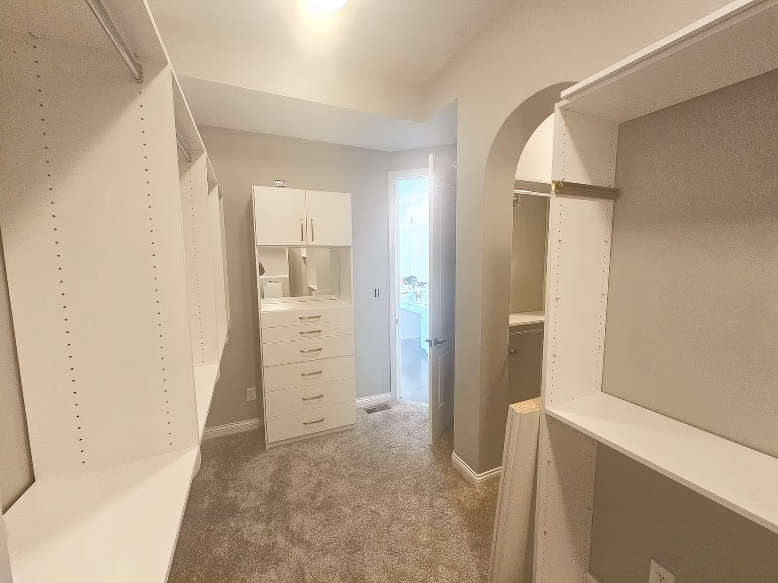 A walk in closet with lots of shelves and a dresser.