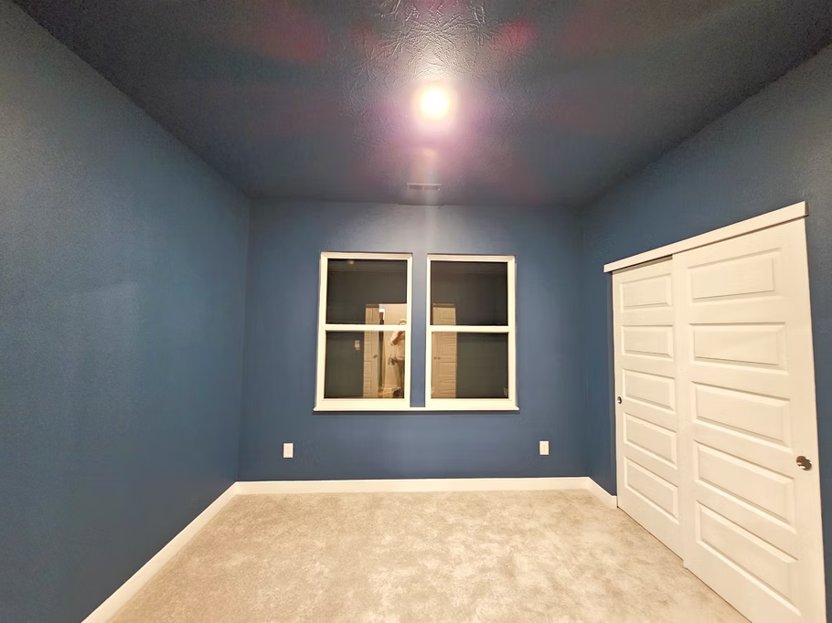 An empty room with blue walls and two windows.
