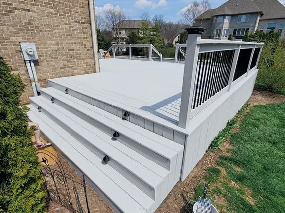 A white deck with stairs and a black railing in front of a brick house.