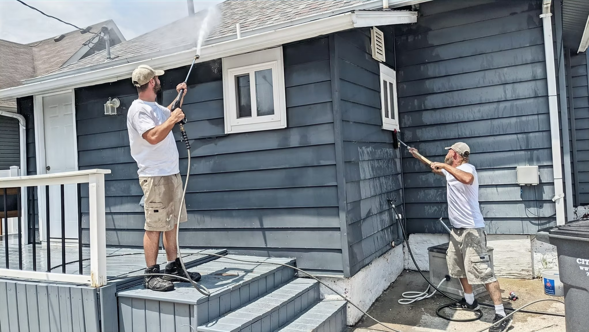 Two men are painting a house with a high pressure washer.