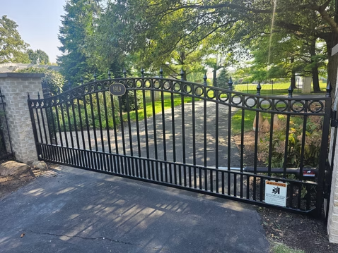 A black wrought iron gate is open to a driveway