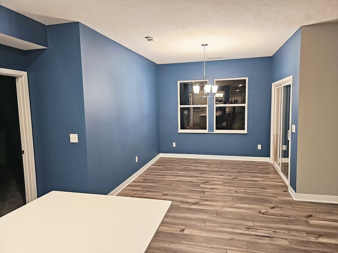 An empty living room with blue walls and wooden floors.