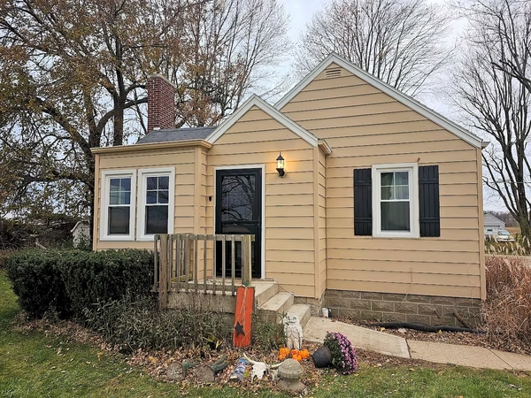 A small yellow house with black shutters and a dog in front of it.