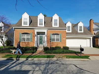 A man walking a dog in front of a large brick house