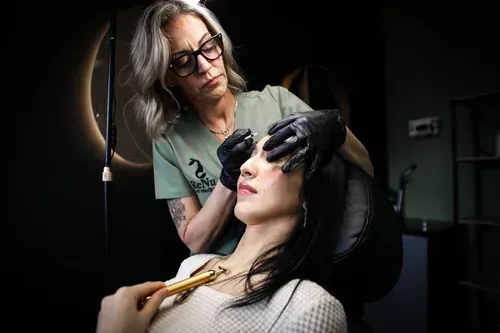 A practitioner giving a facial treatment to a client, indoors, with a focus on eyes.