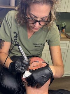 Woman performs cosmetic procedure on another person's face; gloved hands, instrument, focused expression.