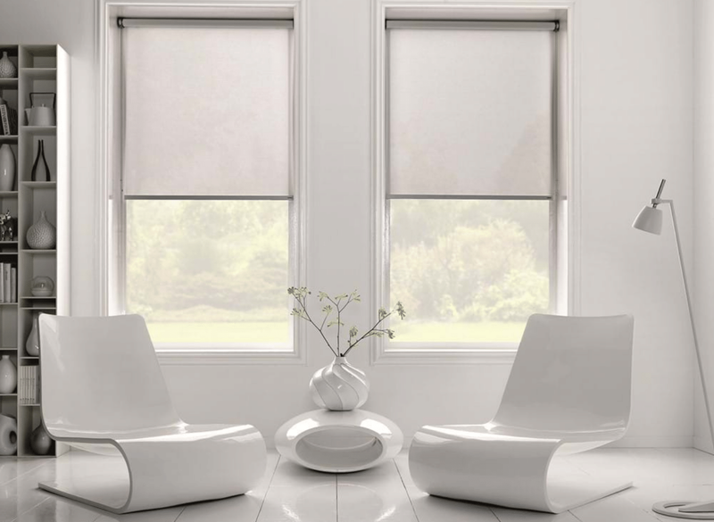 A living room with two white chairs and two windows with blinds.