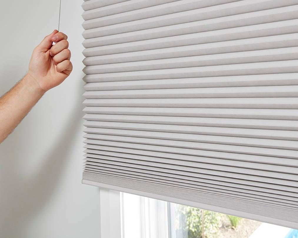 A person is adjusting a honeycomb blind on a window.