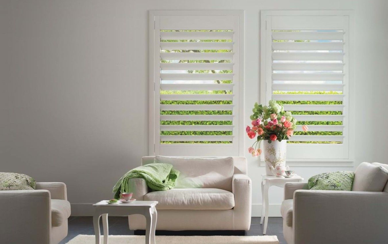 A living room with two white chairs and a white couch and shutters