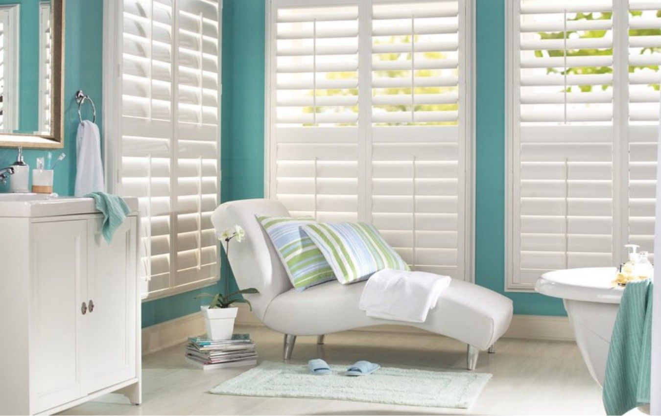 A bathroom with white shutters and a white chaise lounge.