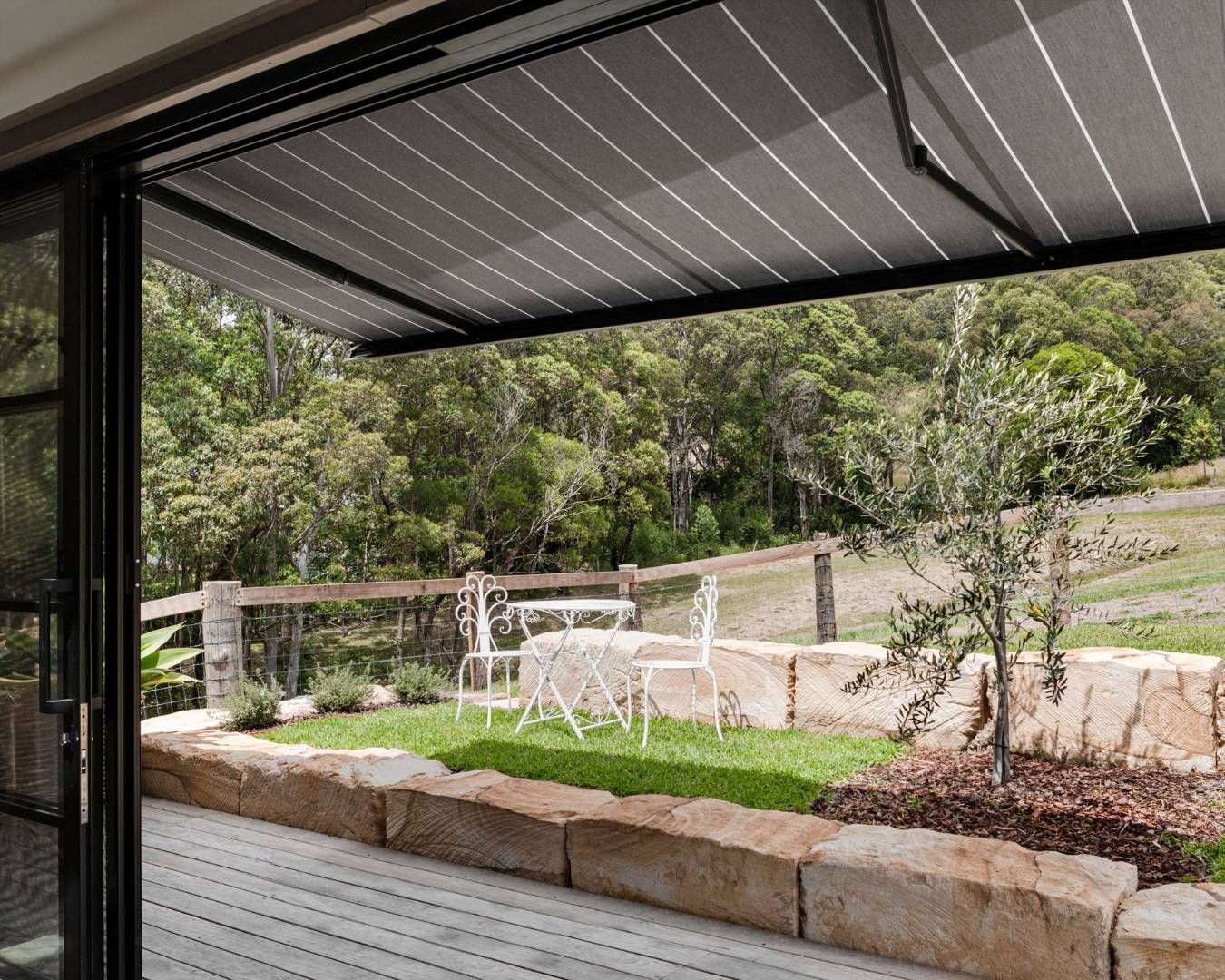 Patio area with a retractable awning, offering shade over a garden seating area with white furniture.