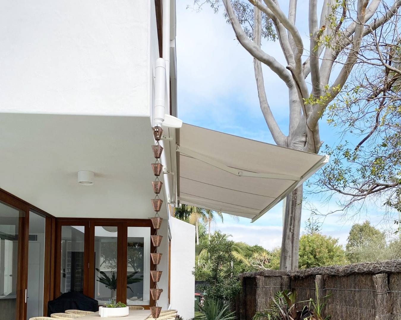 Retractable awning installed on a contemporary white house, providing shade over a patio area.