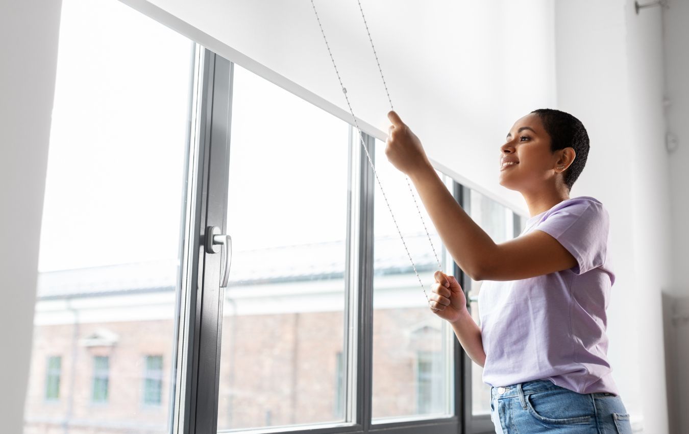 A woman is adjusting a blind on a window.