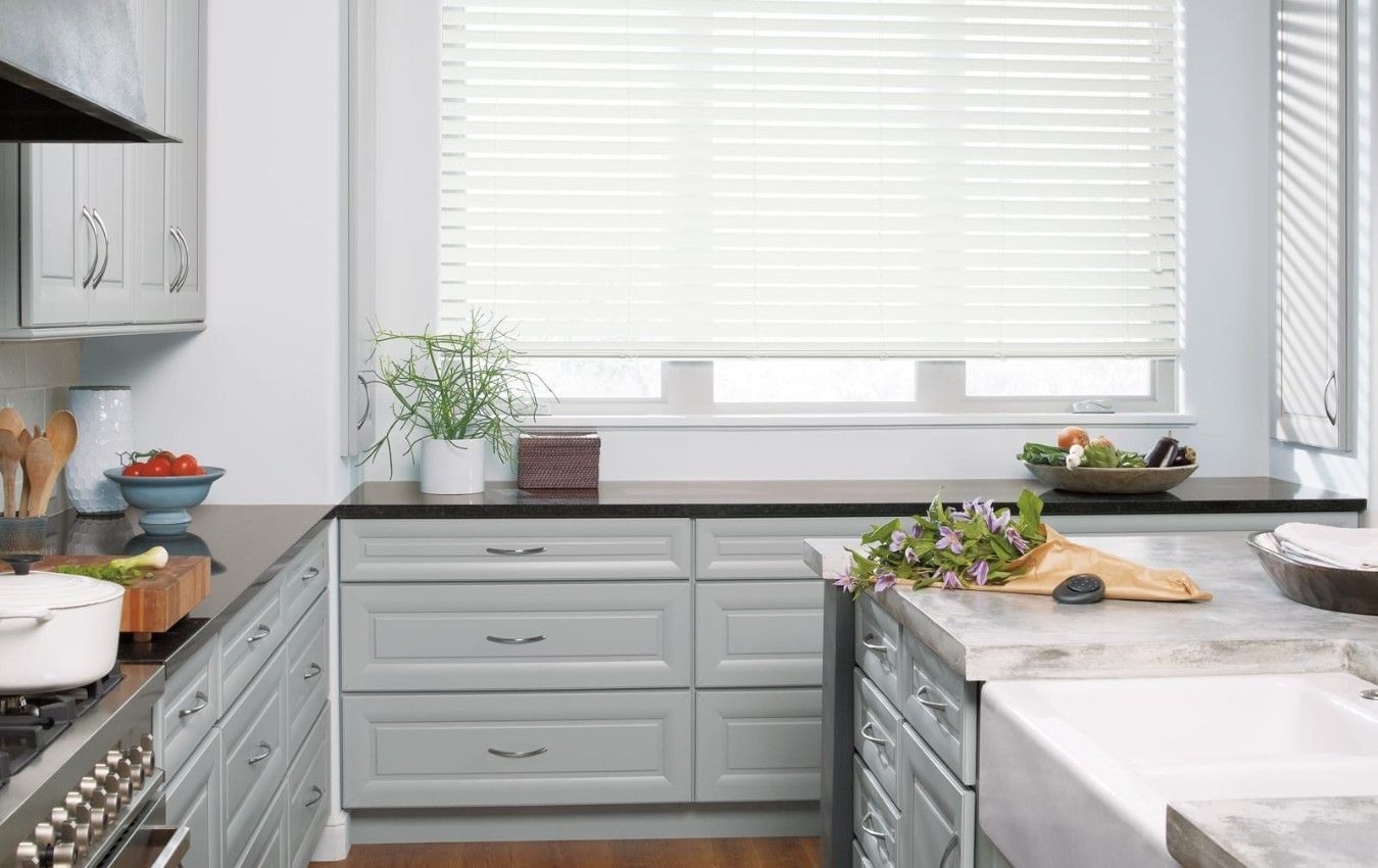 A kitchen with white cabinets , a stove , a sink , and a window.