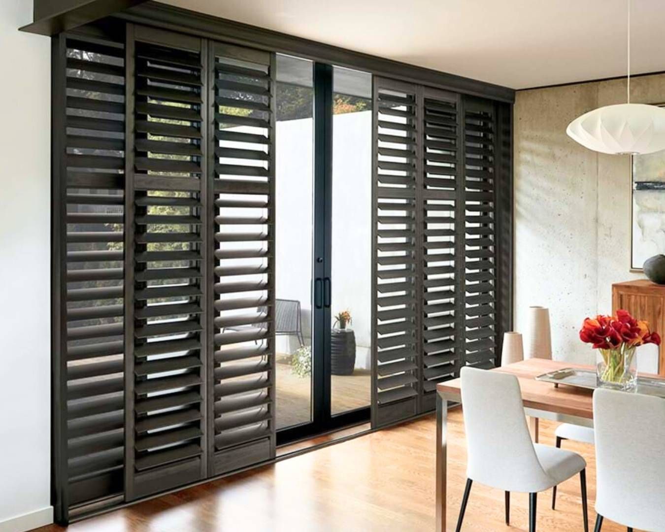 A dining room with a table and chairs and sliding glass doors with shutters.