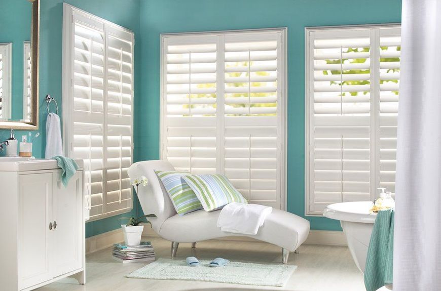 A bathroom with blue walls and white shutters on the windows.