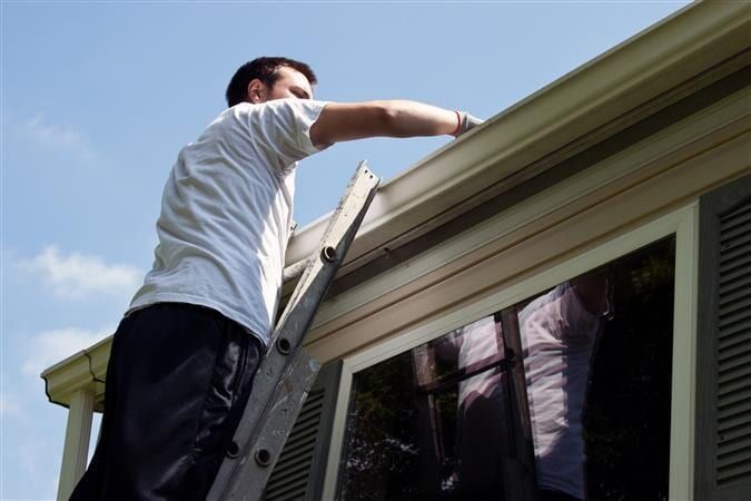 A Man Is Standing On A Ladder Fixing A Gutter On A House — All Style Home Improvements In Hay Point, Qld