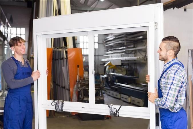 Two Men Are Holding A Large Window In A Factory — All Style Home Improvements in Hay Point, QLD