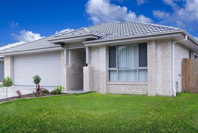 A White Brick House With A White Garage Door And A Large Lawn In Front Of It — All Style Home Improvements in Hay Point, QLD