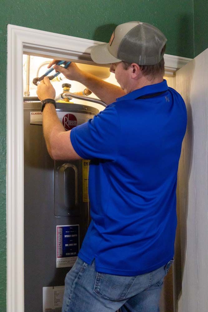 A man in a blue shirt and hat is fixing a water heater.