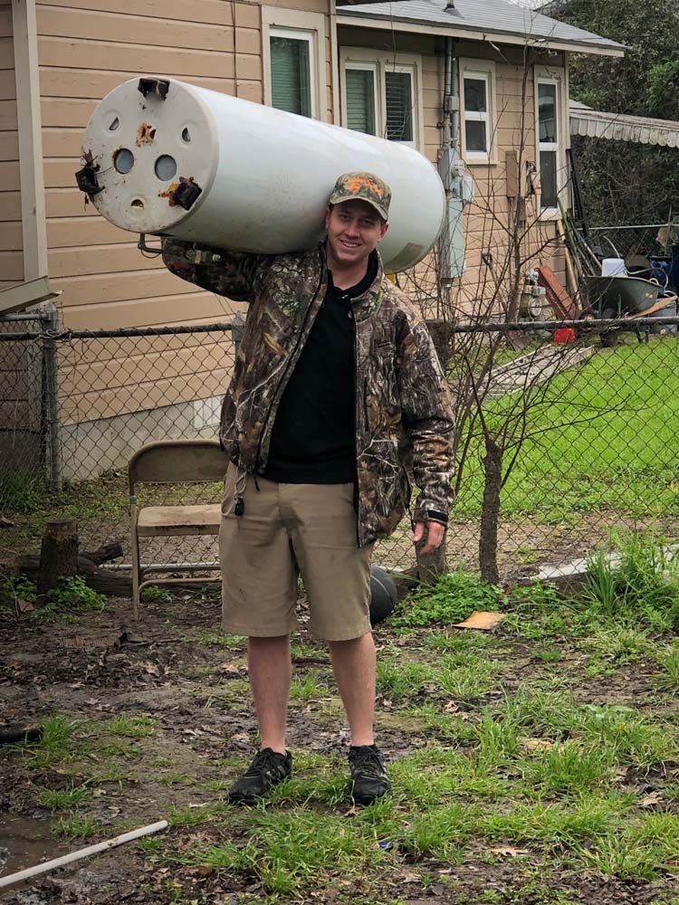 A man is carrying a large water heater on his back.