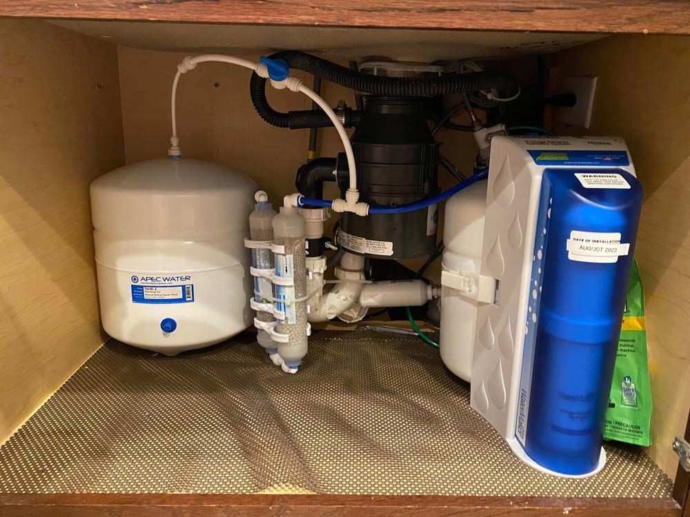 A water filter is sitting under a sink in a cabinet.