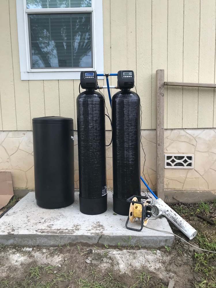 Two black water filters are sitting on a concrete platform in front of a house.