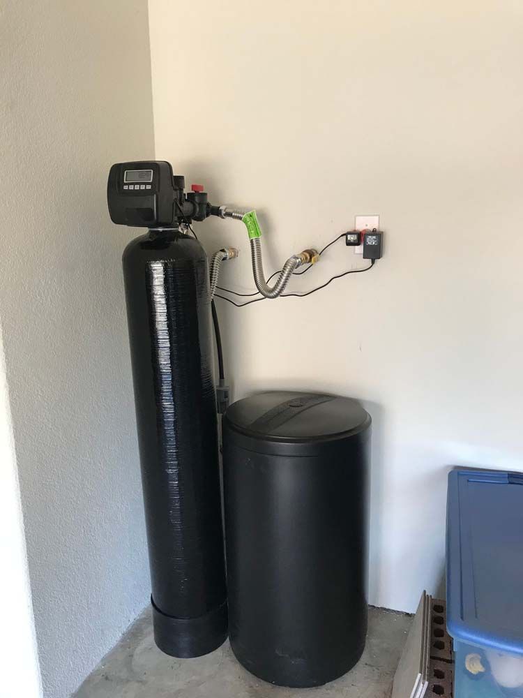A black water softener is sitting next to a black tank in a room.