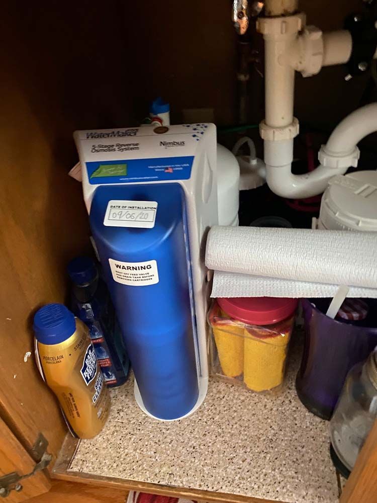 A blue container is sitting under a sink in a cabinet.