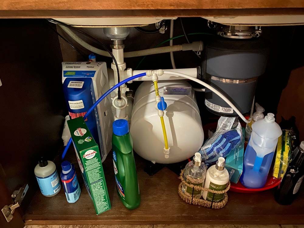 A kitchen sink underneath a cabinet filled with cleaning supplies.